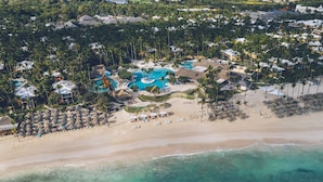 An aerial view of a resort with a central pool, beach area, and dense tropical vegetation.