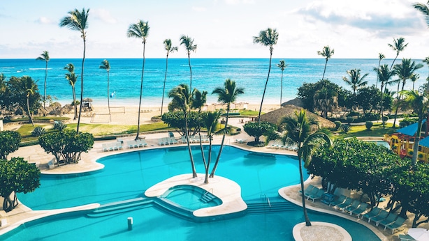 A resort pool with palm trees, lounge chairs, and a view of the ocean.