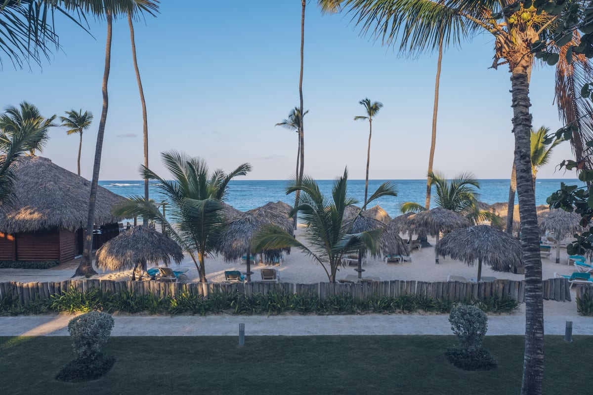 A beach resort with thatched-roof huts, palm trees, and lounge chairs.
