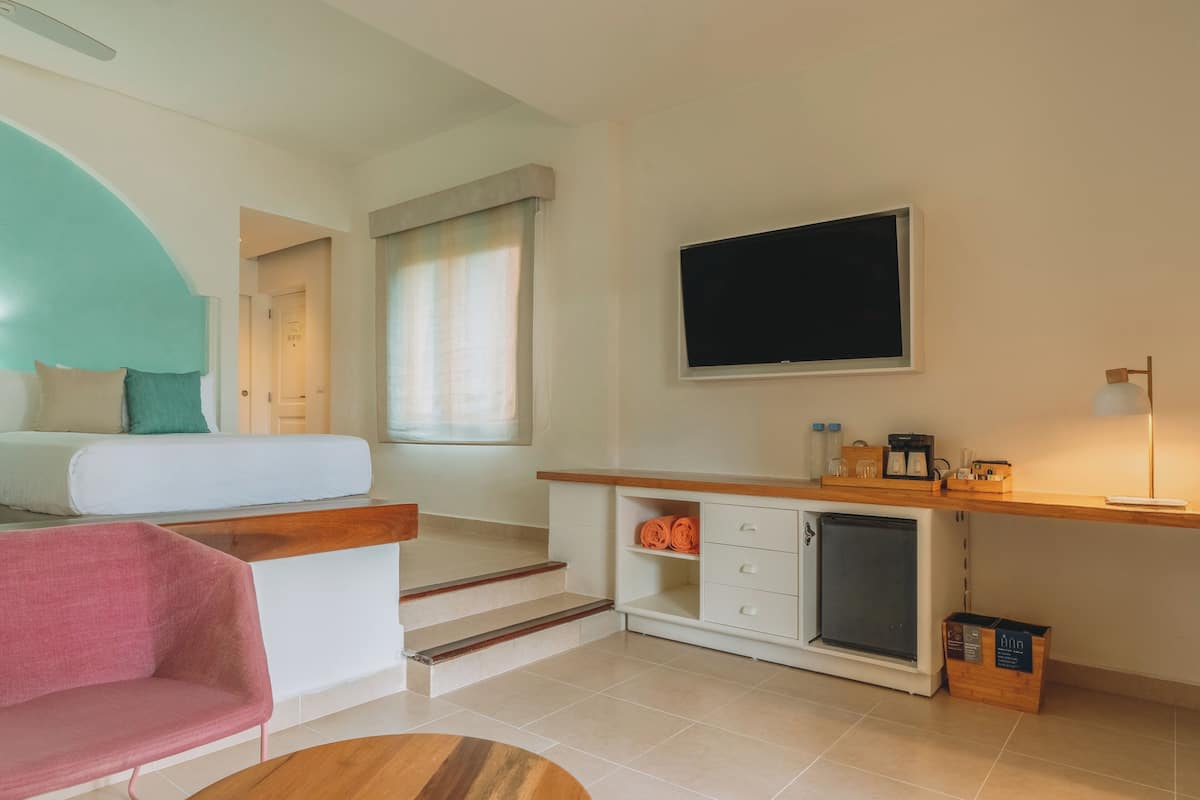 A compact living space with a kitchenette, a TV mounted on the wall, a staircase leading to another room, and a seating area with a chair and a sofa.