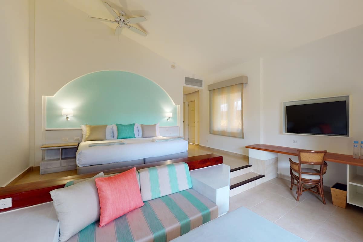 A modern hotel room with a bed, a sofa, a desk, and a TV.