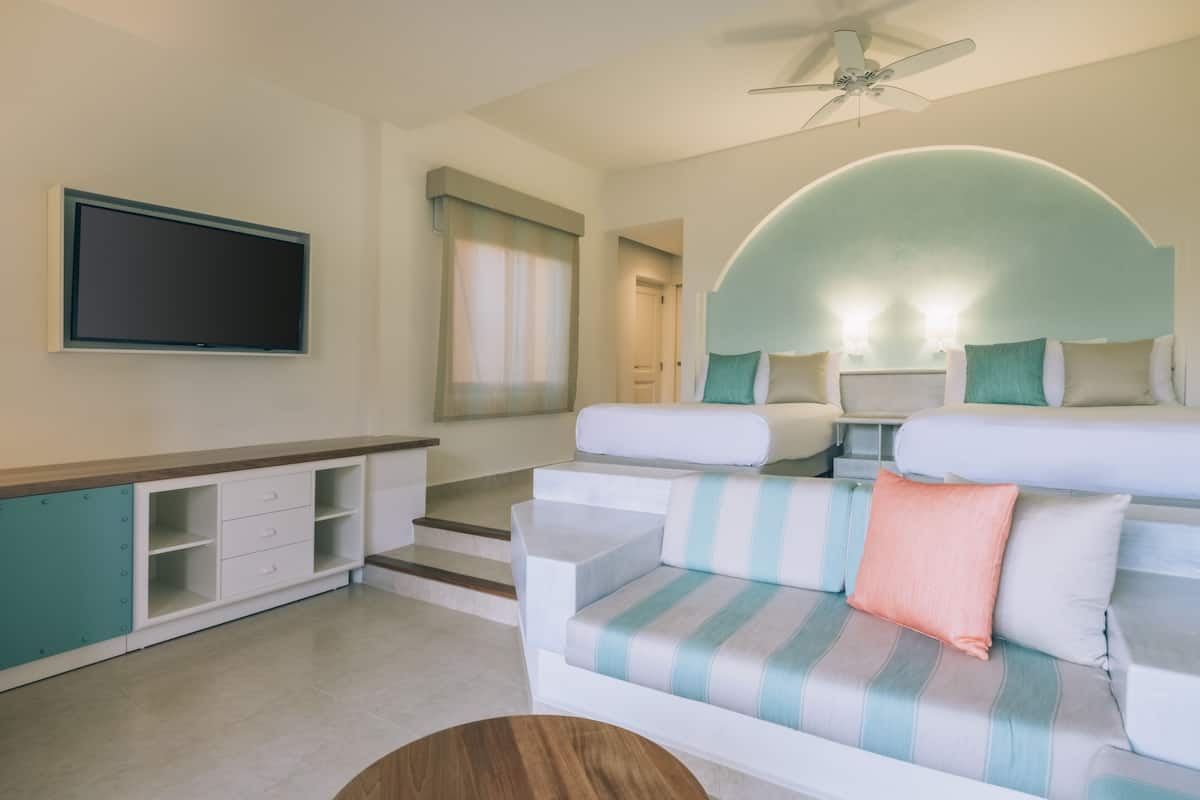 A modern hotel room with a sofa, a TV, a ceiling fan, and a curved wall feature.