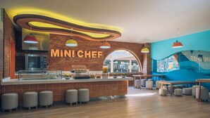 A modern kitchen area with a 'MINICHEF' sign, a counter with food display, and seating arrangements.