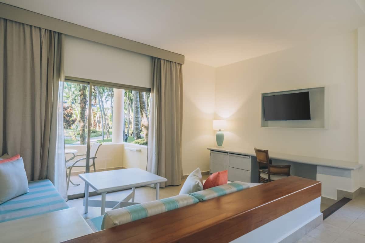 A hotel room with a sofa, a table, a TV mounted on the wall, and a view of the outdoors.
