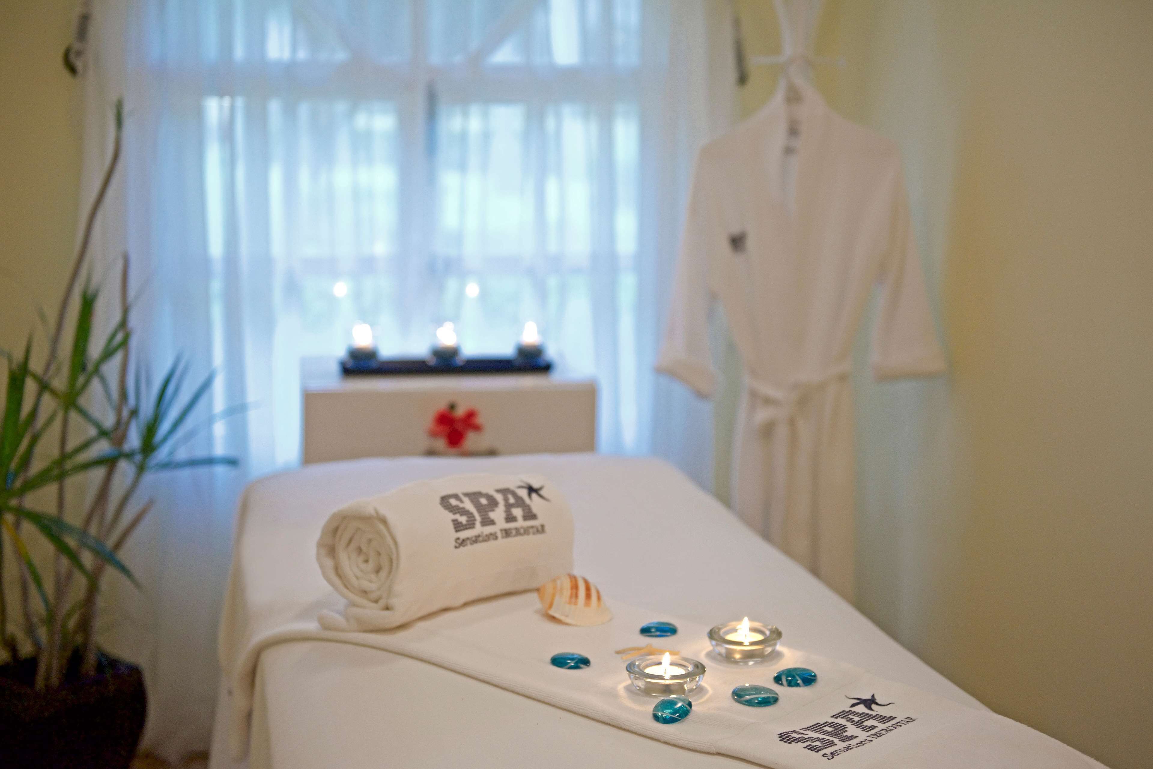 A spa room with a bed, candles, a towel with 'SPA' text, and a robe hanging on the wall.