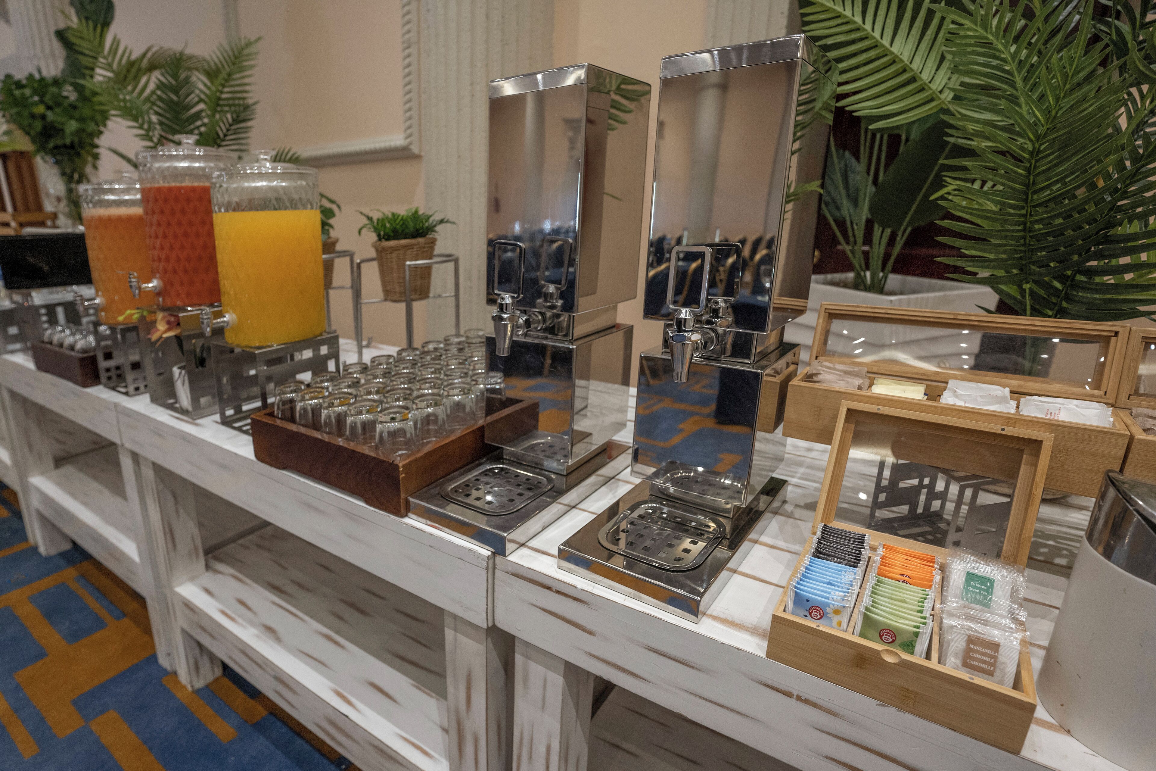 A buffet setup with juice dispensers, a variety of glasses, and a tray with condiments.