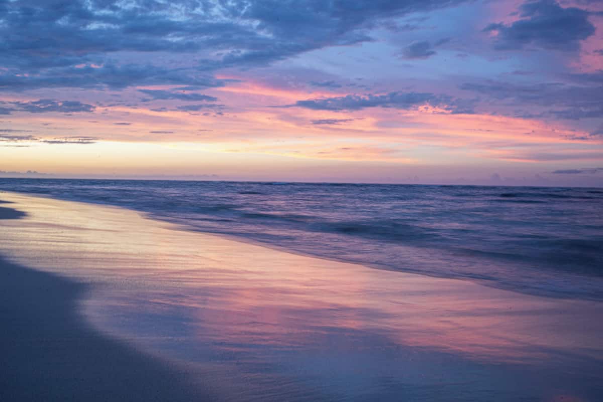 A beach with a calm sea and a sunset sky.