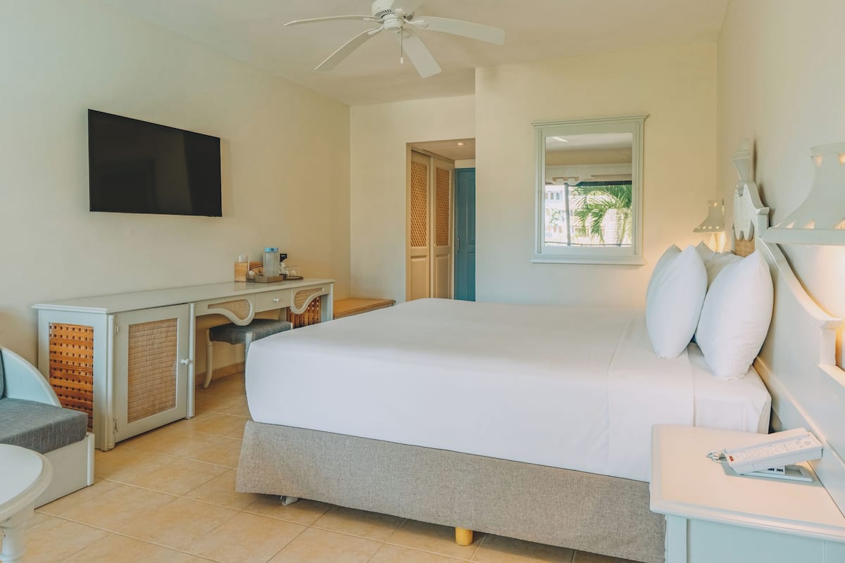 A bedroom with a bed, a desk, a chair, a TV, and a window with a view.