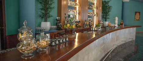 A bar area with a marble countertop, glass jars of snacks, and a variety of bottles and glasses on shelves.
