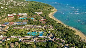 An aerial view of a resort with multiple buildings, a large swimming pool, and a beach.
