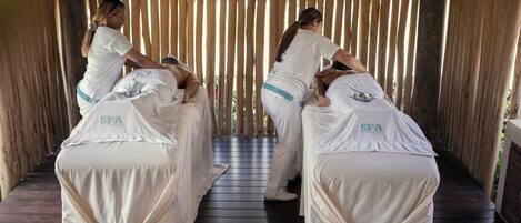 A spa treatment room with two massage tables, each covered with a white cloth and a spa logo.