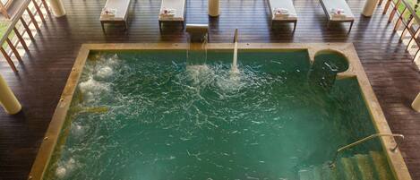 Ein Whirlpool mit Wasserdüsen, umgeben von Liegestühlen und einer Holzterrasse.