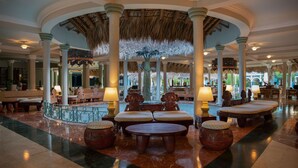 A spacious lobby with a central seating area, columns, and a thatched ceiling.