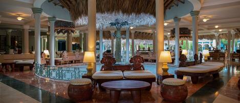 A spacious lobby with a central seating area, columns, and a thatched ceiling.