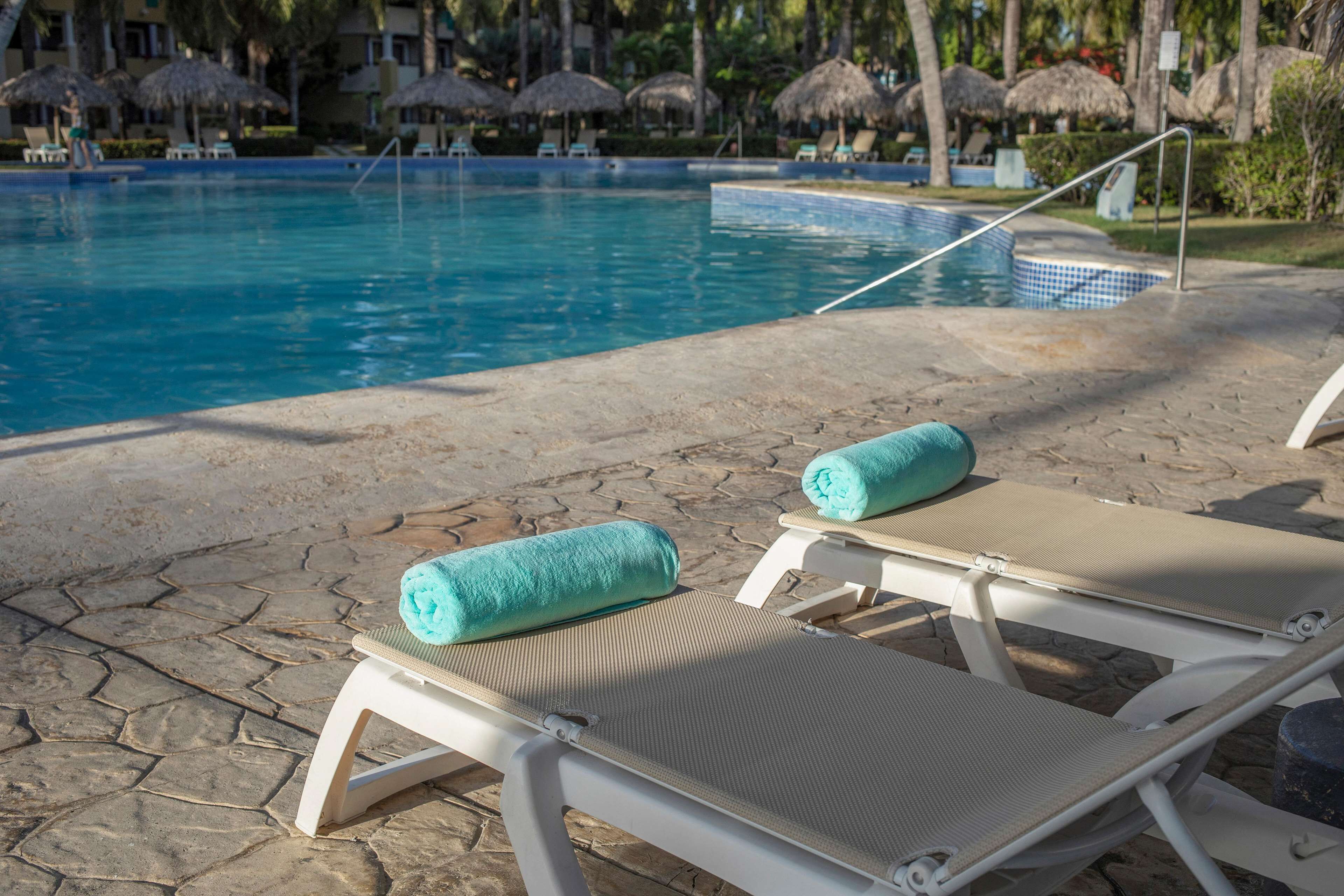 A poolside area with lounge chairs and towels, a small hot tub, and thatched umbrellas.