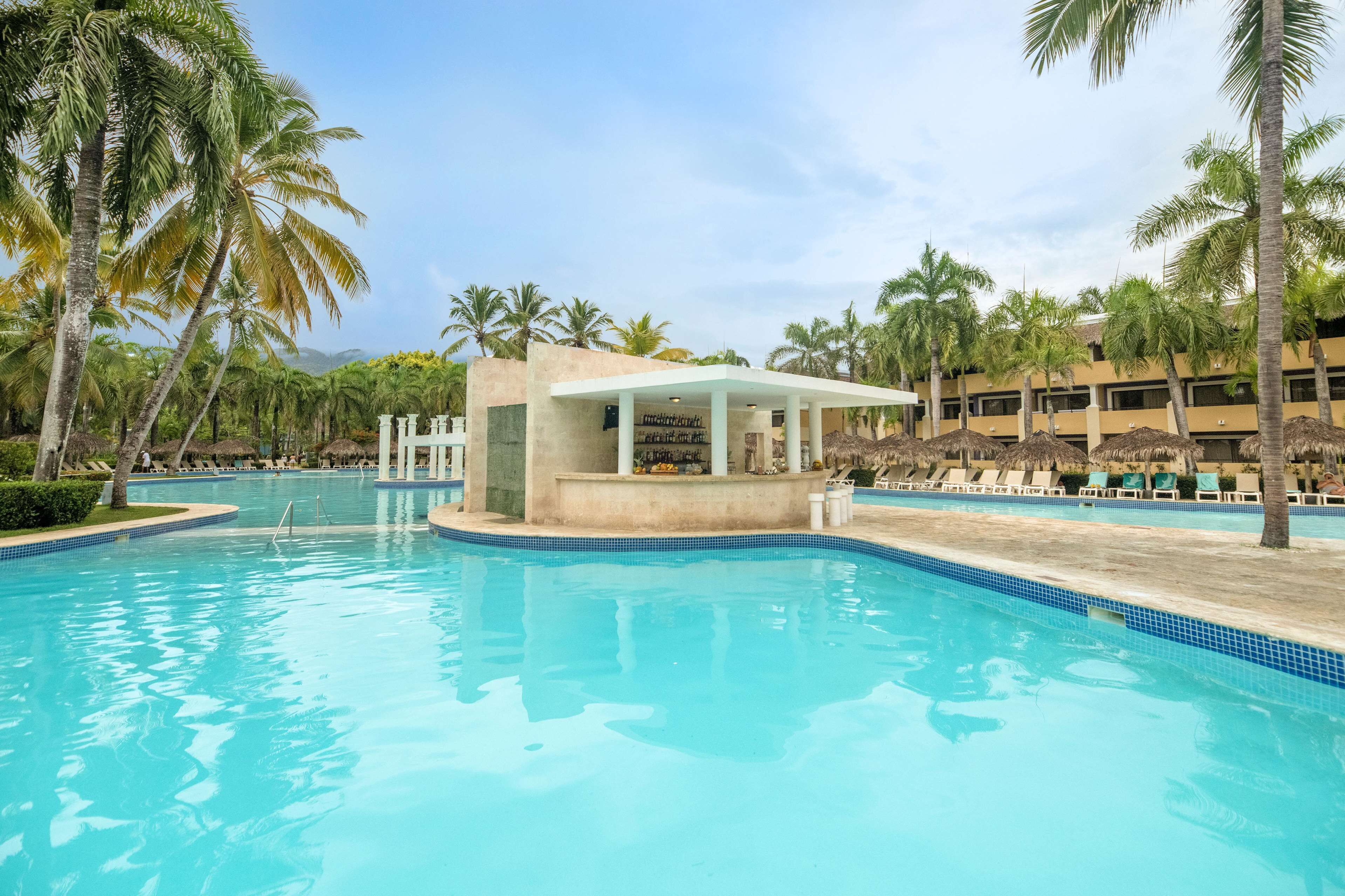 A swimming pool with a bar area, surrounded by palm trees and lounge chairs.