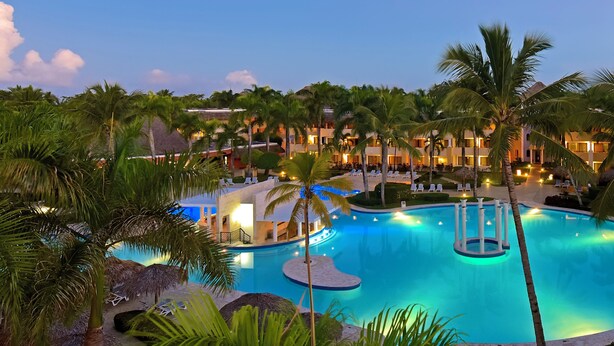 A resort pool with palm trees, lounge chairs, and a building with multiple balconies.