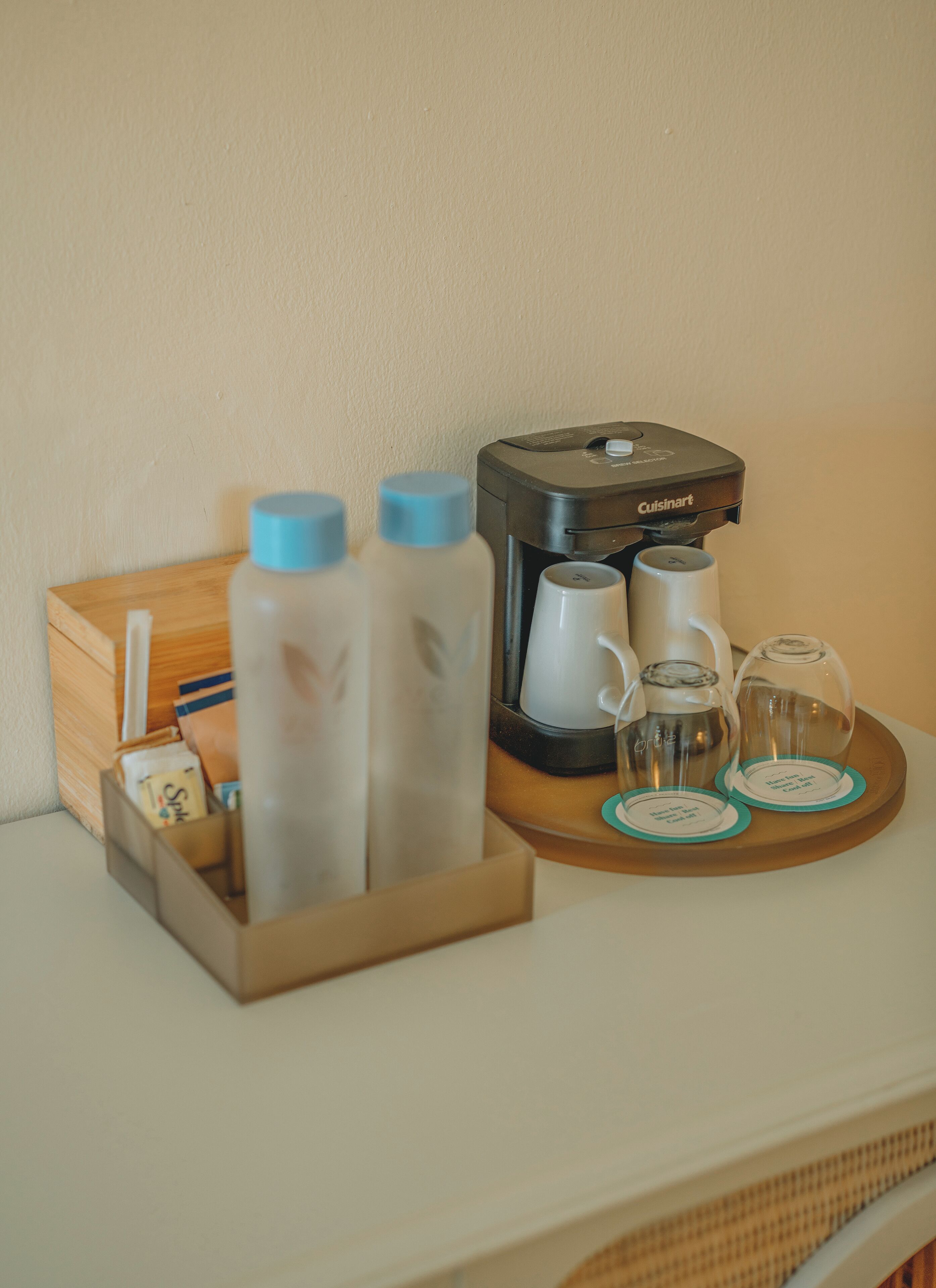 Una cafetera, dos botellas de agua, una tetera y una bandeja con dos vasos sobre una superficie de madera.