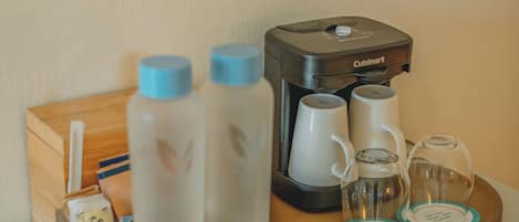 A coffee maker, two water bottles, a tea kettle, and a tray with two glasses on a wooden surface.