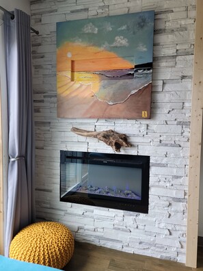 A room with a stone wall, a painting of a sunset, a television, and a wooden bench. - Chautauqua Resort & Conference Center (Long Beach)