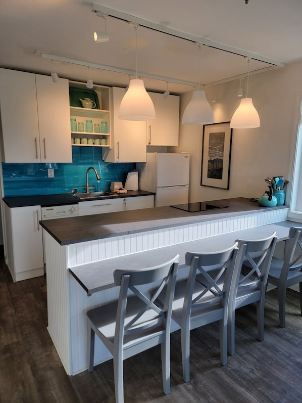 A modern kitchen with a central island, white cabinetry, a blue backsplash, and pendant lighting.