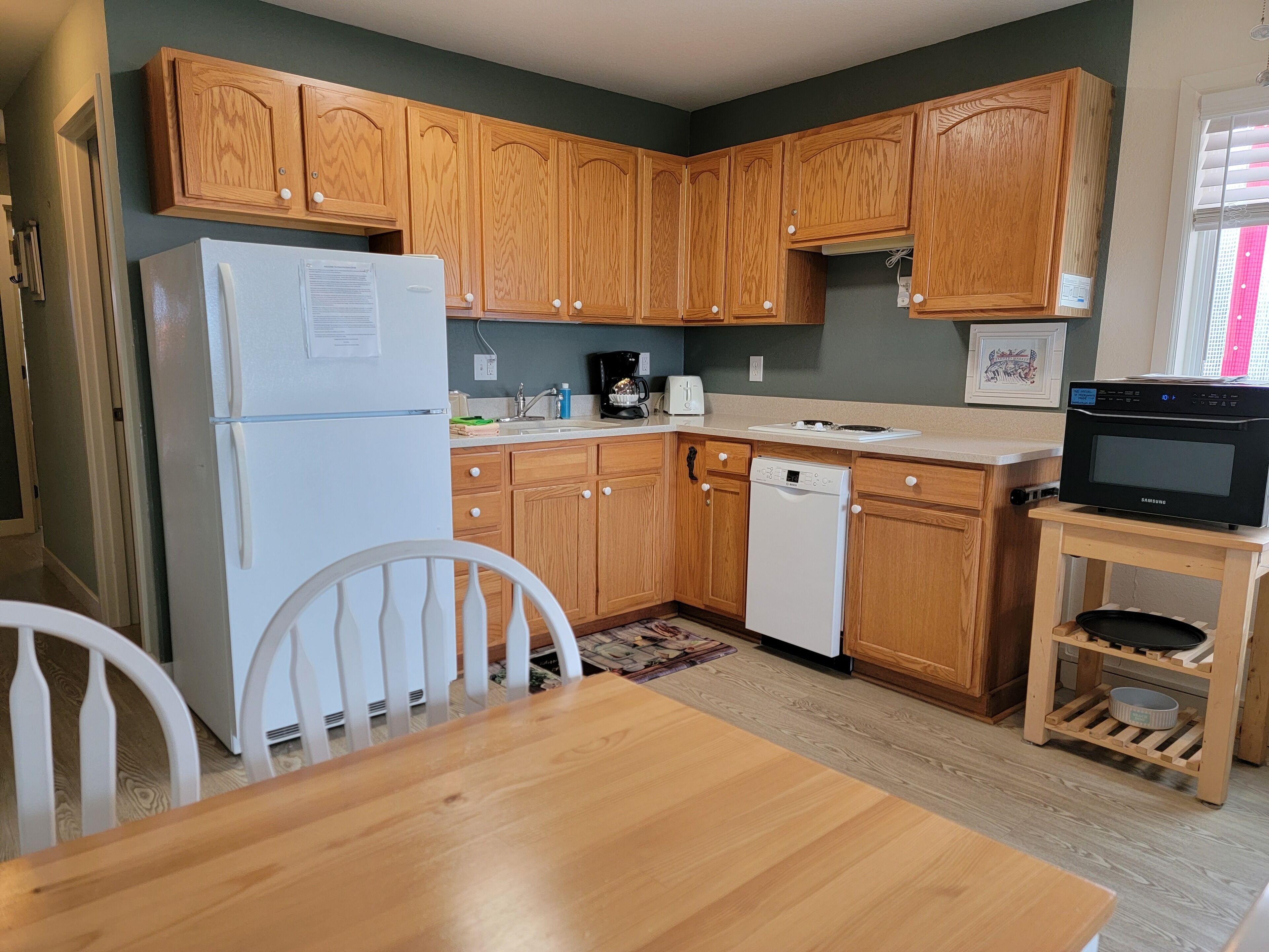 A compact kitchen with wooden cabinets, a white refrigerator, a dishwasher, a microwave, and a dining area with a wooden table and chairs.