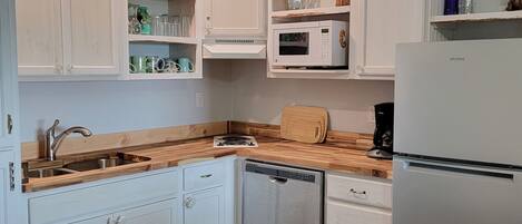 Una cucina con mobili bianchi, un piano di lavoro in legno, lavastoviglie, forno a microonde e frigorifero.