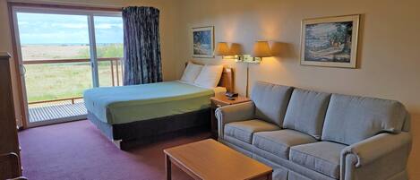 A hotel room with a bed, a sofa, a table, and a balcony with a view of the beach.
