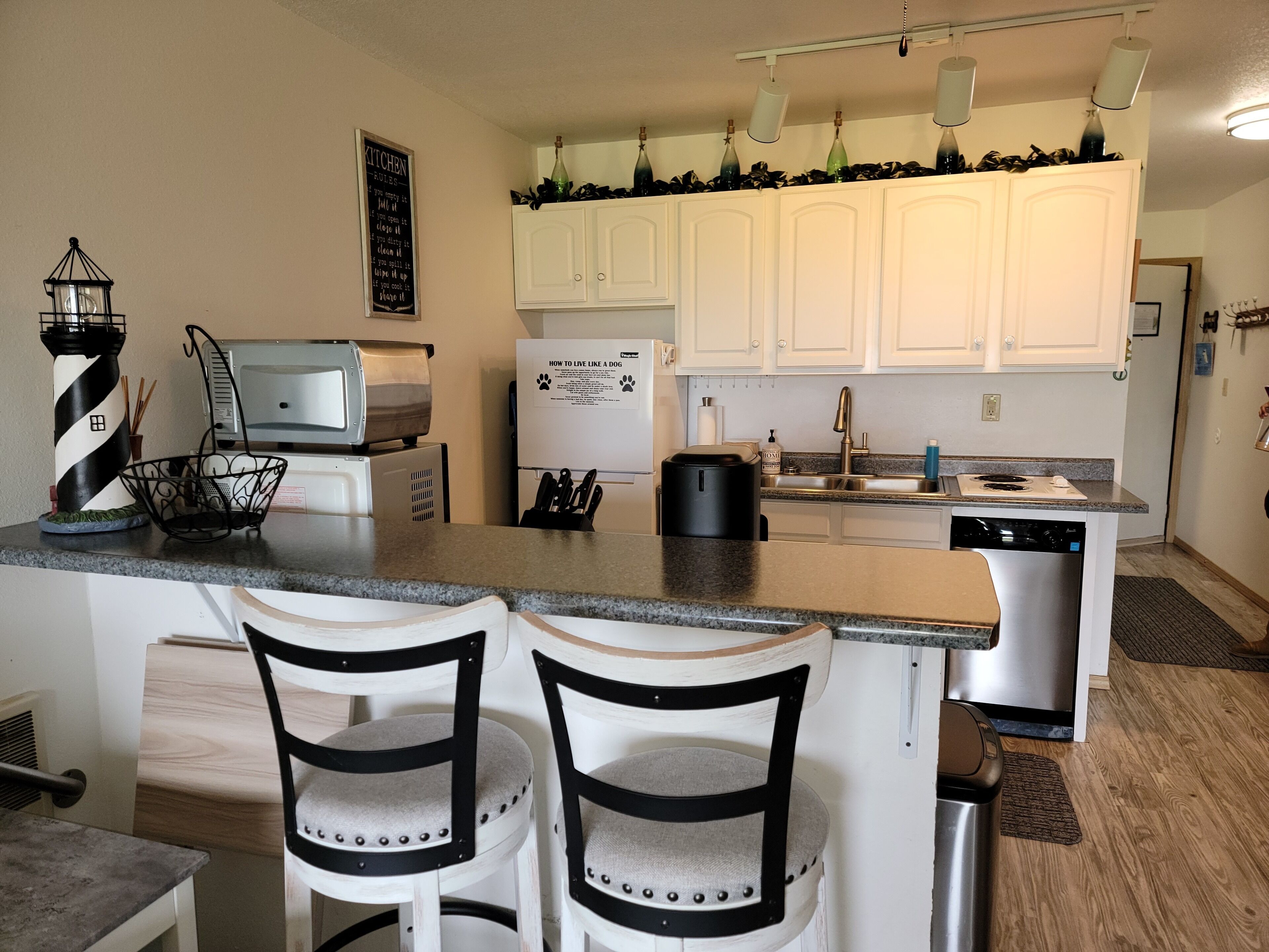 A modern kitchen with white cabinets, a granite countertop, a microwave, a coffee maker, and two bar stools.