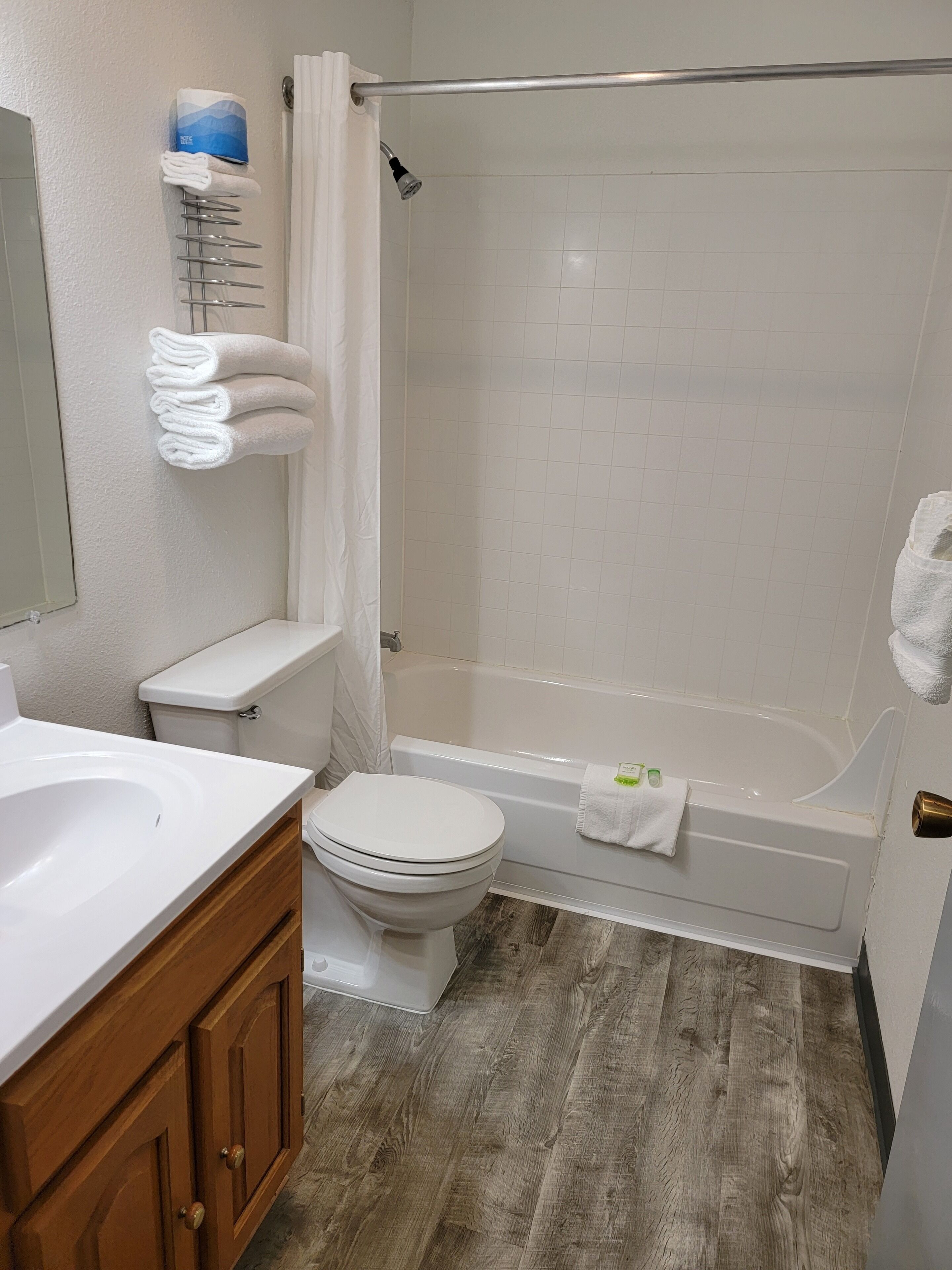 Une salle de bain avec des toilettes, un lavabo et une baignoire. Des serviettes sont suspendues sur un porte-serviettes et il y a un rideau de douche.
