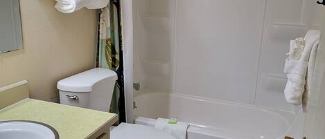 A bathroom with a toilet, sink, and bathtub. There is a towel rack with folded towels, a shower curtain, and a small stool with a decorative item.