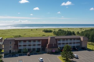A hotel with a parking lot, a view of the ocean, and a grassy area.