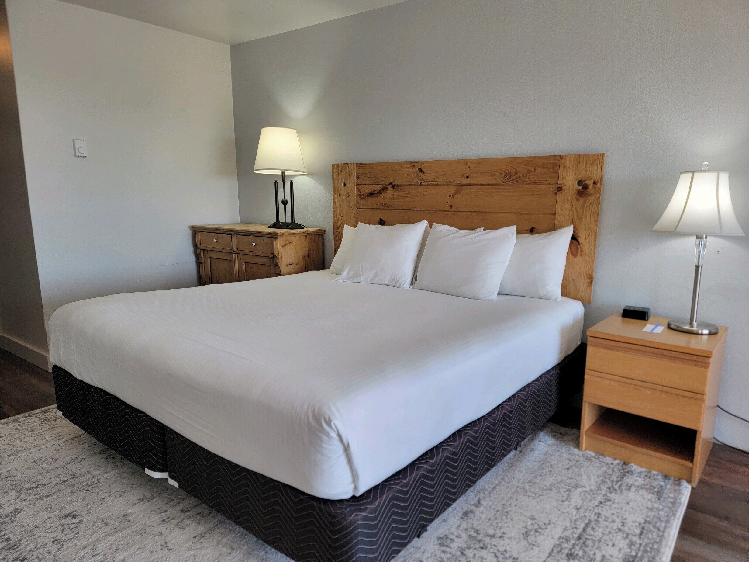 A neatly made bed with a wooden headboard, two bedside tables with lamps, and a patterned rug.