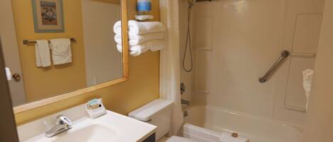 A bathroom with a sink, toilet, and bathtub. There is a towel rack with towels, a mirror, and a sign above the bathtub that says "DRIP DRY".