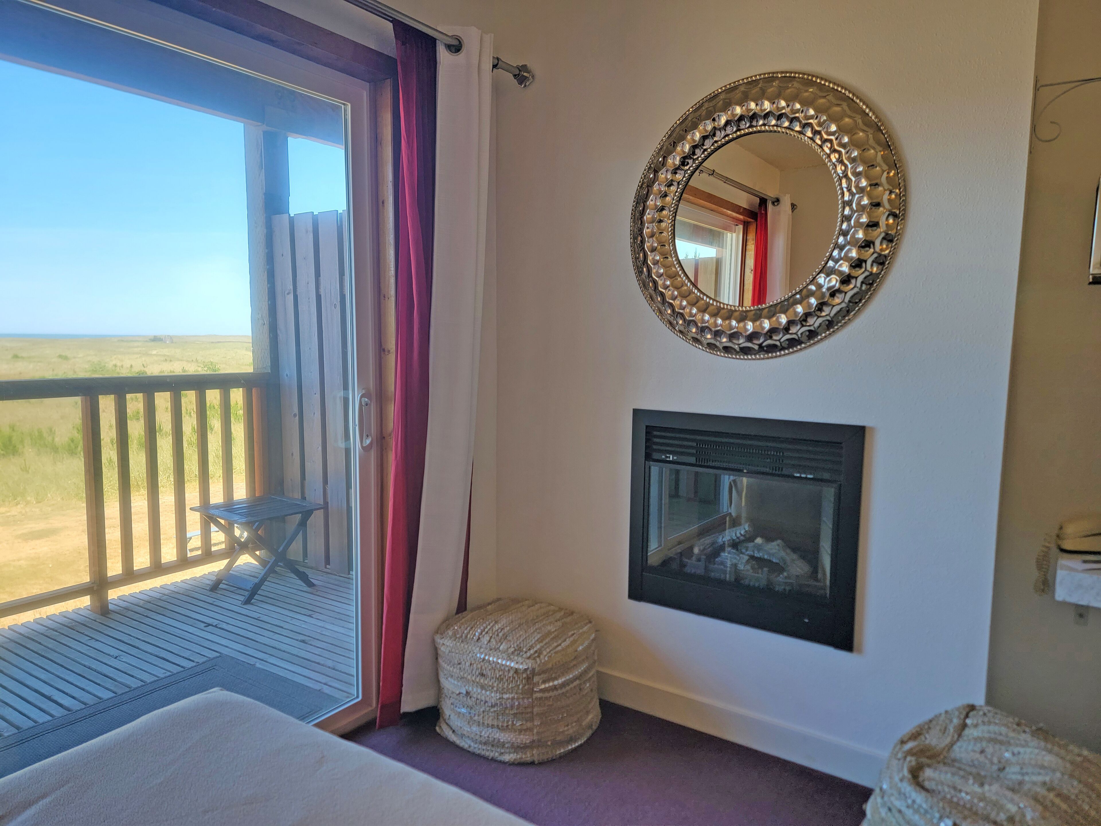 Una habitación con un ventanal grande, un espejo, una chimenea y un pequeño taburete.