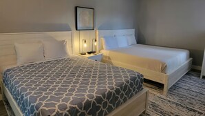 Una cama doble con una colcha estampada, una mesita de noche con una lámpara y un cuadro enmarcado en la pared.
