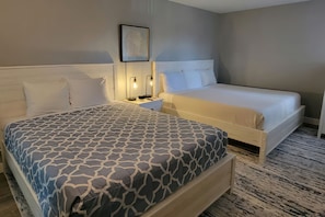A double bed with a patterned bedspread, a bedside table with a lamp, and a framed picture on the wall.