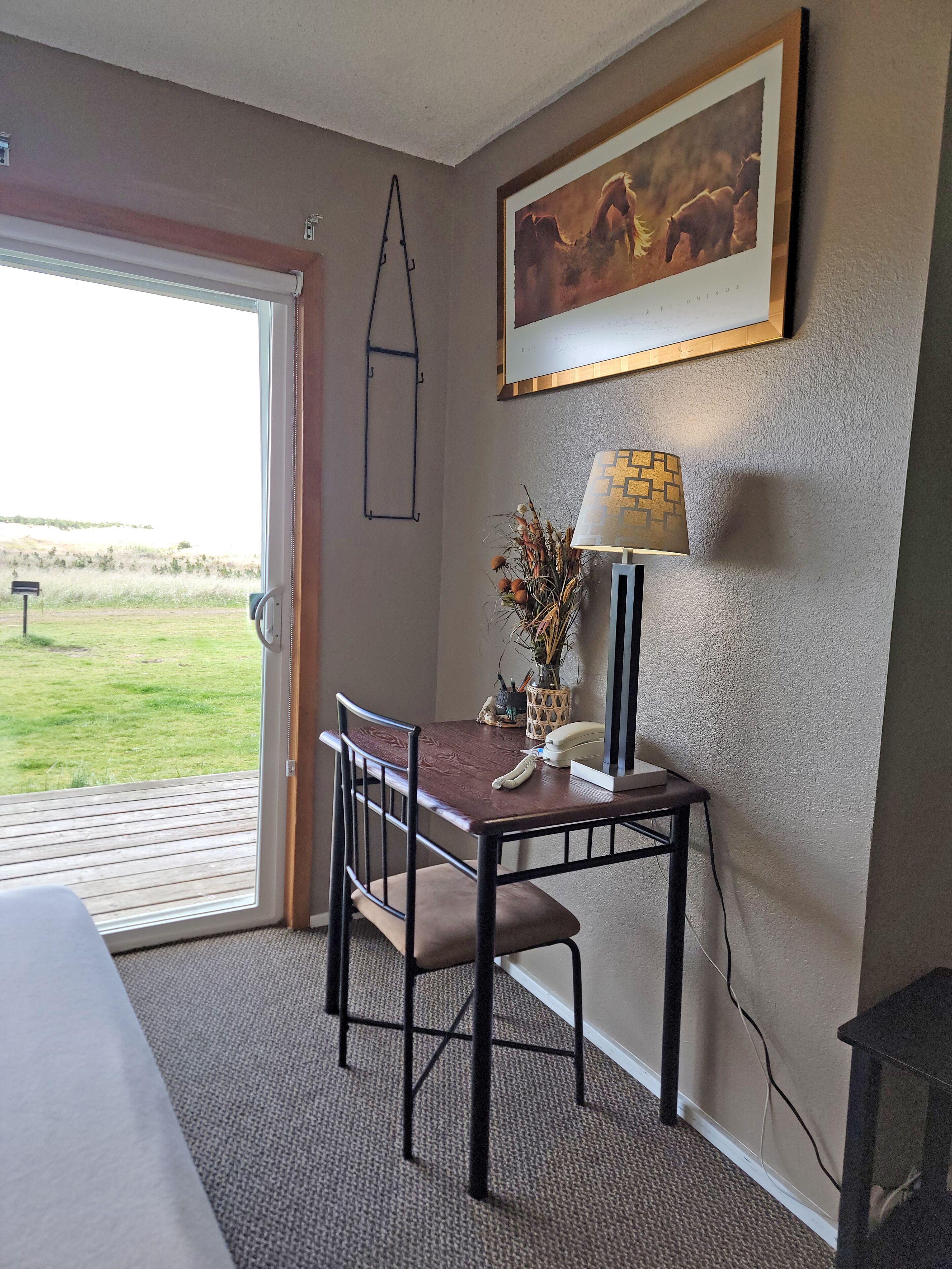 A room with a wooden dining table, two chairs, a lamp, and a framed picture on the wall.