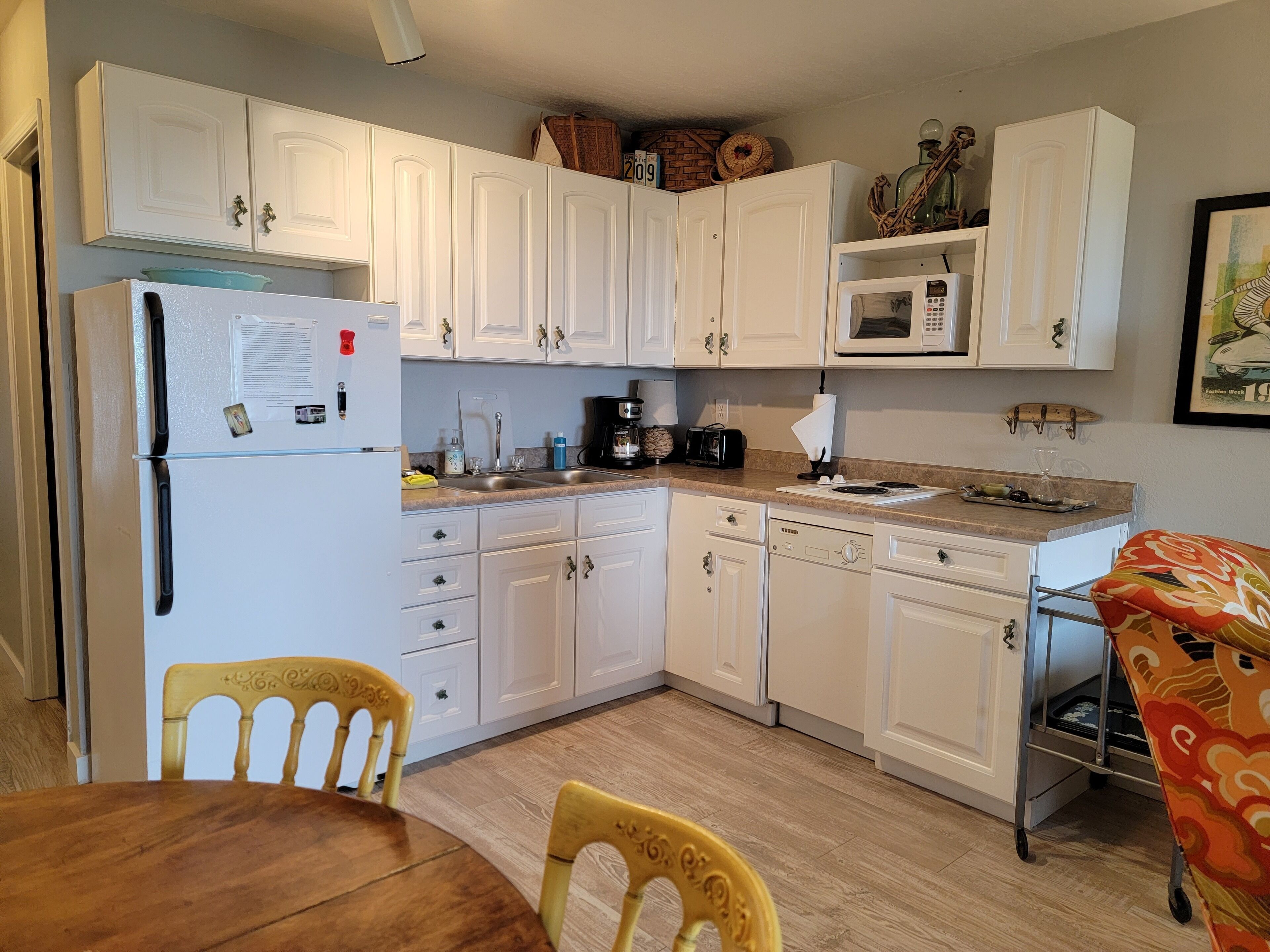 A compact kitchen with white cabinets, a refrigerator, a microwave, and a dining area with a wooden table and chairs.