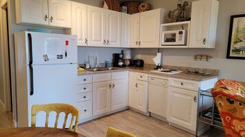 A compact kitchen with white cabinets, a refrigerator, a microwave, and a dining area with a wooden table and chairs.