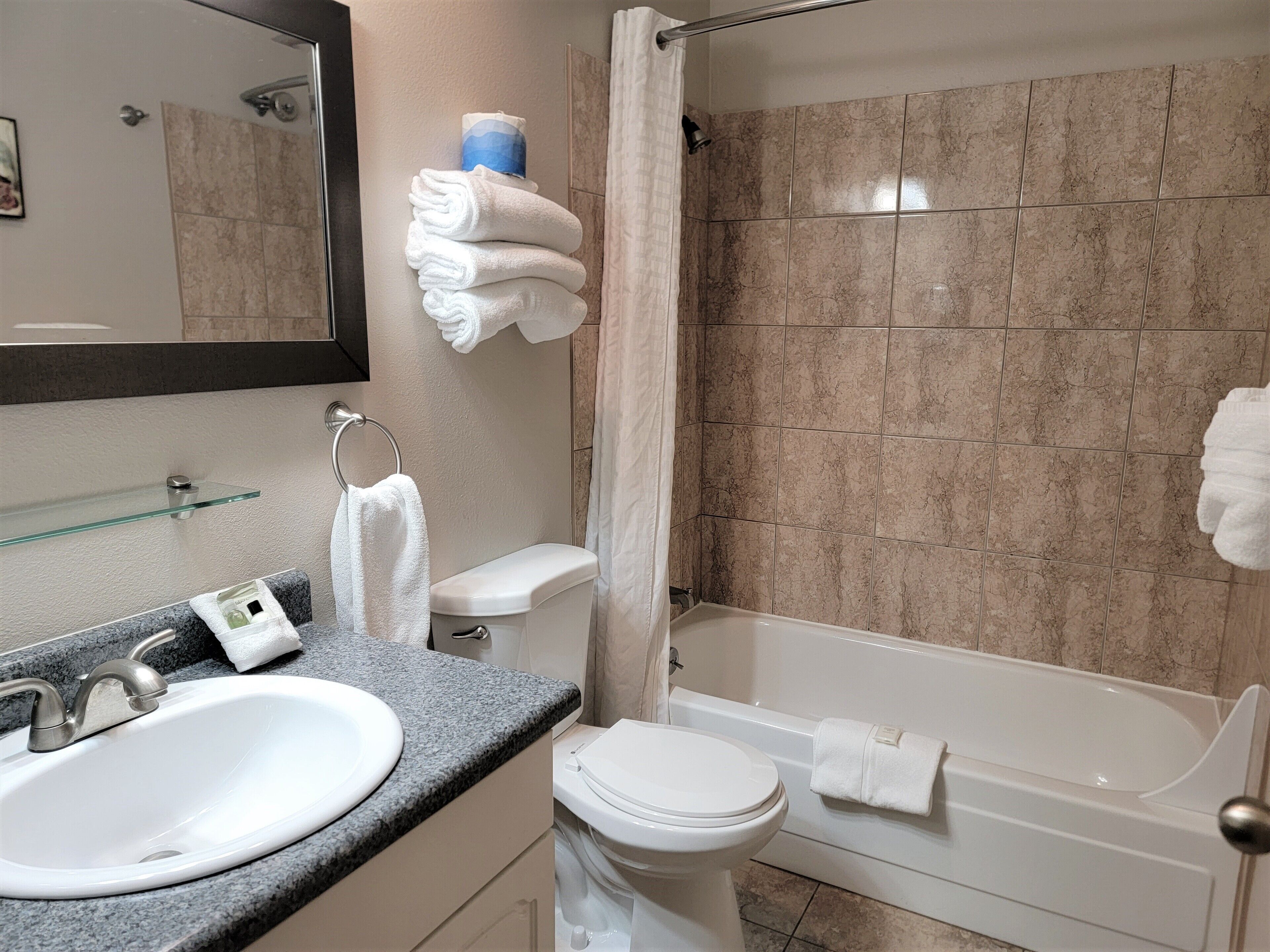 A bathroom with a sink, toilet, and bathtub. There are towels stacked on a shelf and a glass shower enclosure.
