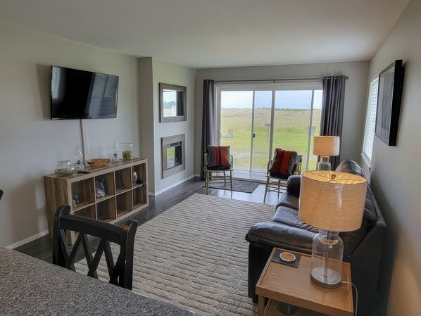 A living room with a flat-screen TV, a fireplace, a sofa, and a view of the outdoors.