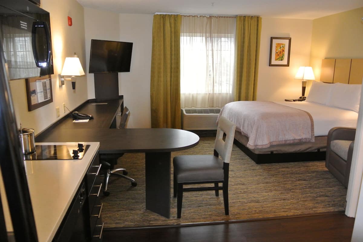 Une chambre d’hôtel comprenant un lit, un bureau avec une chaise, une télévision, une fenêtre avec des rideaux et un appareil de climatisation.