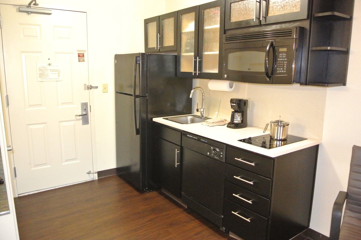 A compact kitchen with black cabinets, a stainless steel refrigerator, a microwave, and a coffee maker.