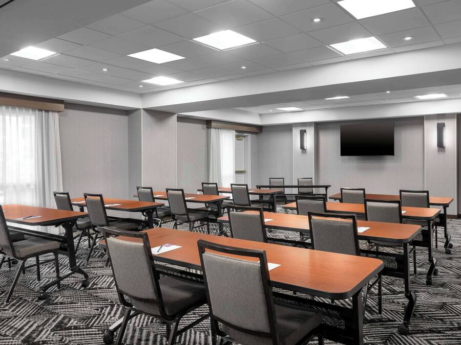 Une salle de conférence dotée de plusieurs tables et chaises, d’un téléviseur à écran plat fixé au mur et d’un sol recouvert de moquette.