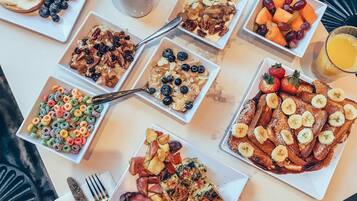 Un bufé de desayuno con diversos platos, incluyendo panqueques, gofres, cereales y fruta.