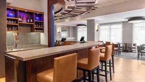 Een bar met een toonbank, krukken en flessen op de planken.