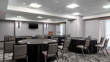 A conference room with multiple round tables, chairs, a flat-screen TV, and a carpeted floor.
