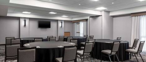 A conference room with multiple round tables, chairs, a flat-screen TV, and a carpeted floor.