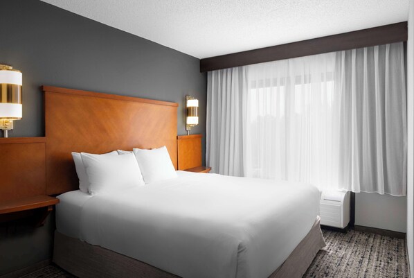 A hotel room with a large bed, wooden headboard, two bedside tables with lamps, a large window with sheer curtains, and a carpeted floor. - Hyatt Place Dallas-North/by the Galleria (Dallas)